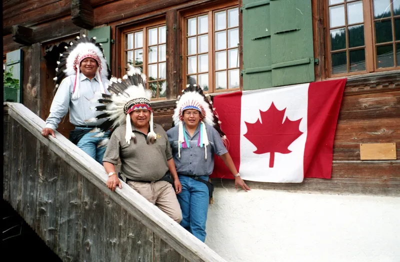 Trois leaders autochtones en coiffes de plumes sur un balcon de bois, à côté d’un drapeau canadien
