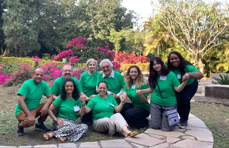 Nine participants in green IofC T-shirts holding hands on the lawn at Asia Plateau