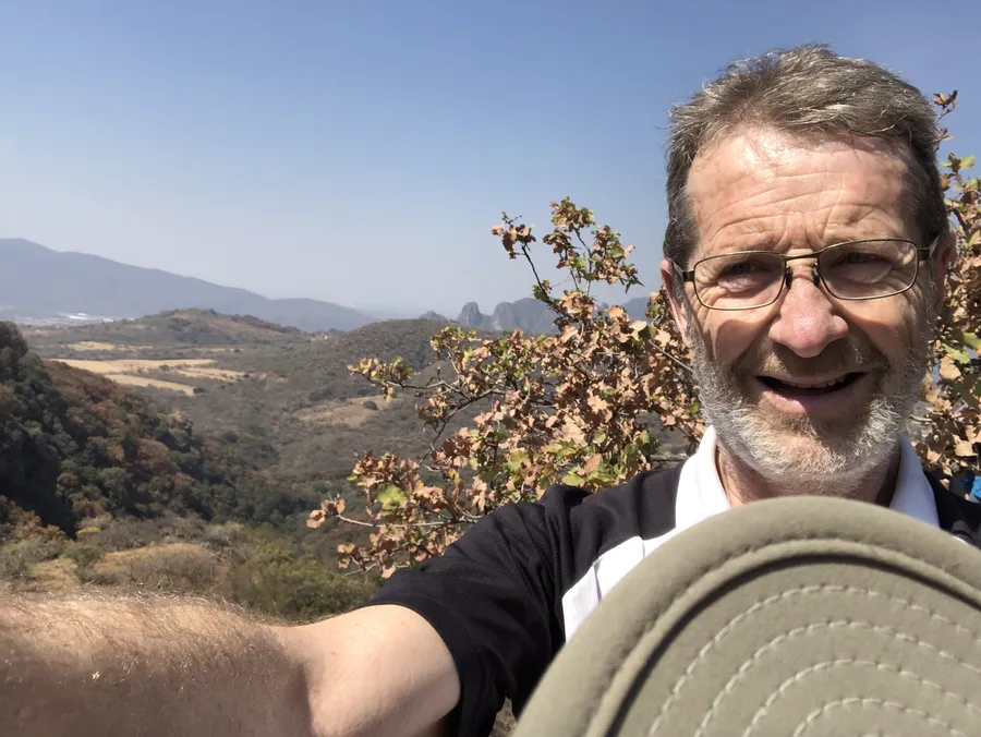 David Swann smiling on a hillside, dry mountains behind him