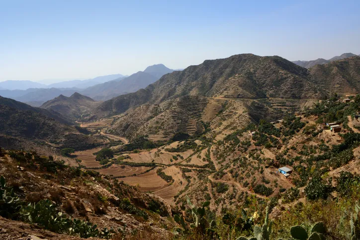 Terraced hills and mountains in Eritrea under a hazy sky, a road winding through the valley