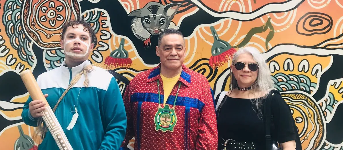 Three participants standing in front of a painted mural at the Global Indigenous Dialogue in Australia