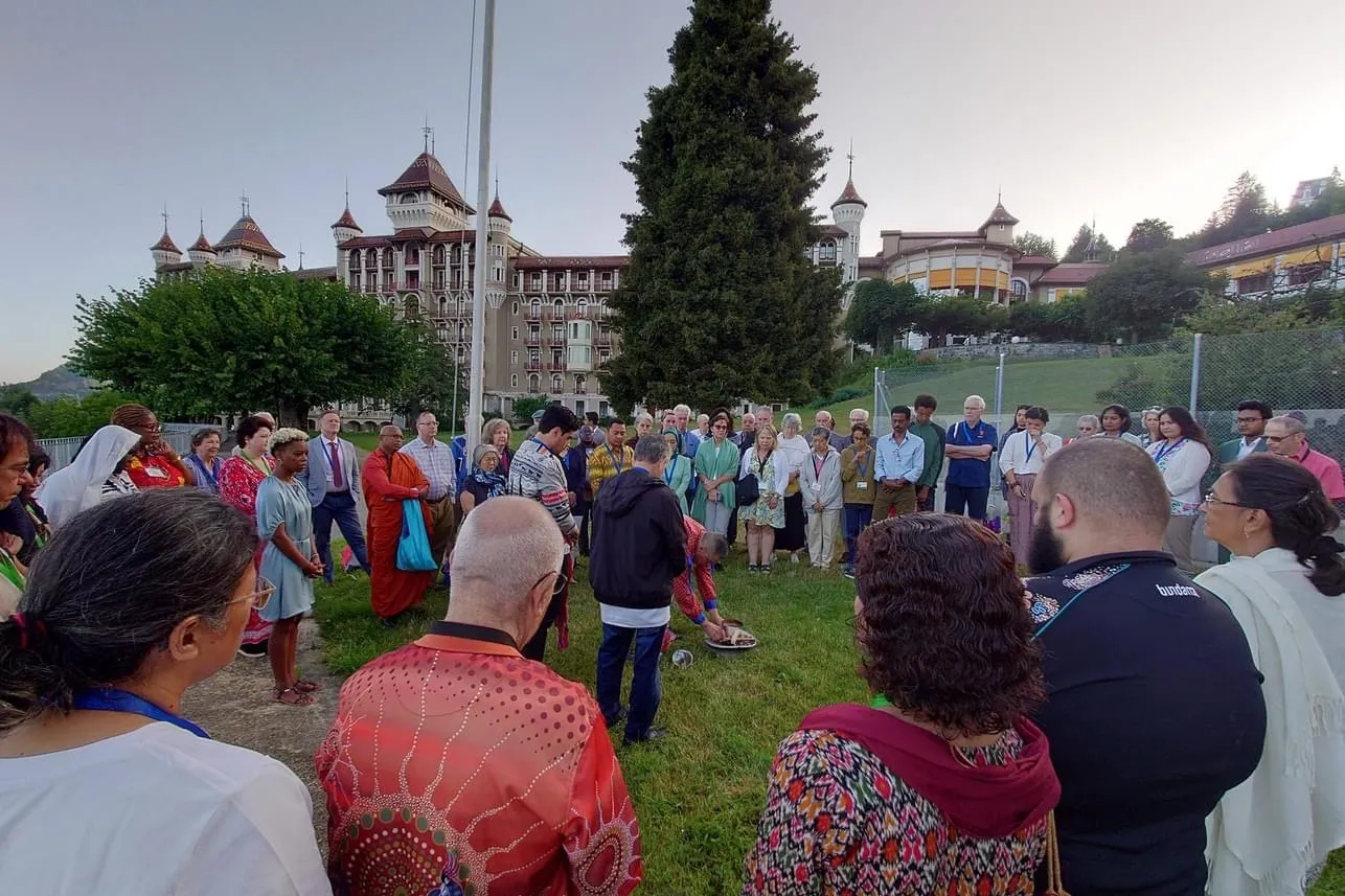 A circle of participants standing on the lawn in front of the Caux Palace at the Caux Forum 2023