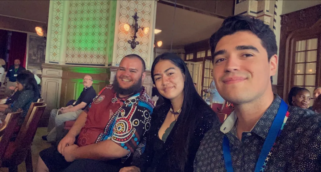 Three young participants seated in the Caux conference hall, smiling at the camera