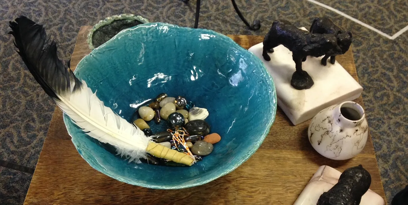 A turquoise bowl holding stones and a feather on a wooden table